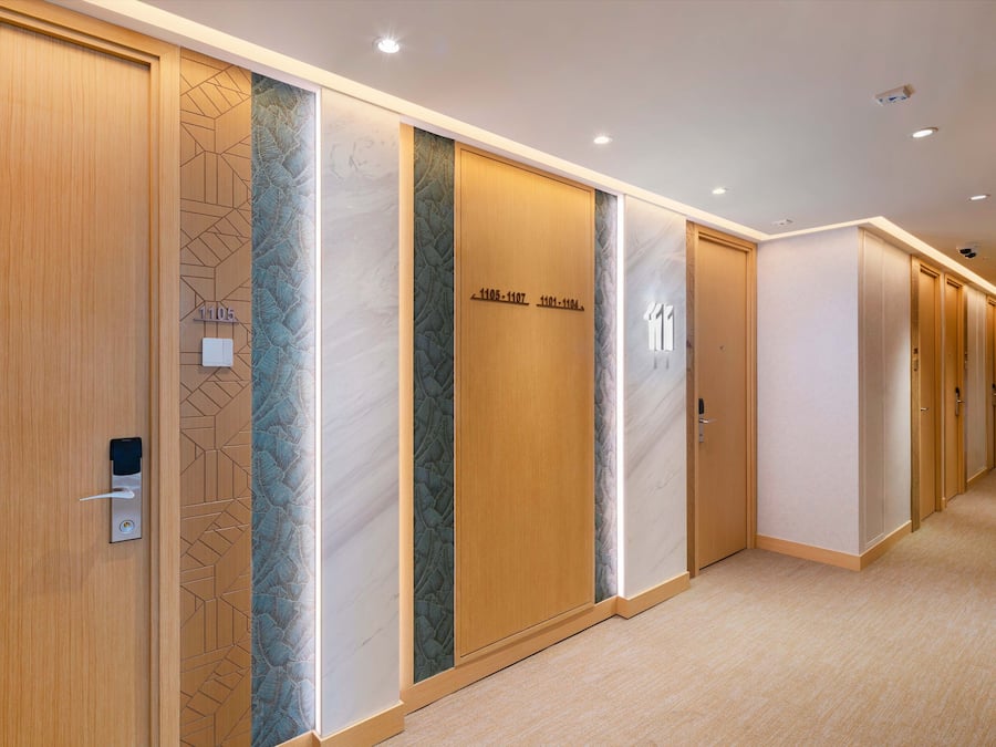 A hotel corridor with wooden doors, numbered room signs, and a carpeted floor.