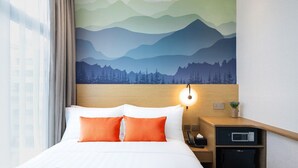 Een hotelkamer met een bed, nachtkastje, lamp en een wanddecoratie van bergen.