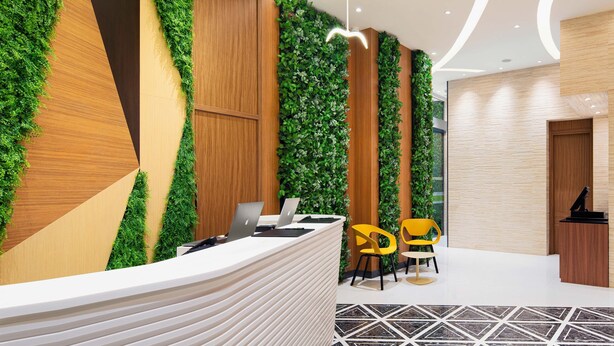 Een modern ingerichte receptie met een receptiebalie, twee gele stoelen en een wand begroeid met groen.