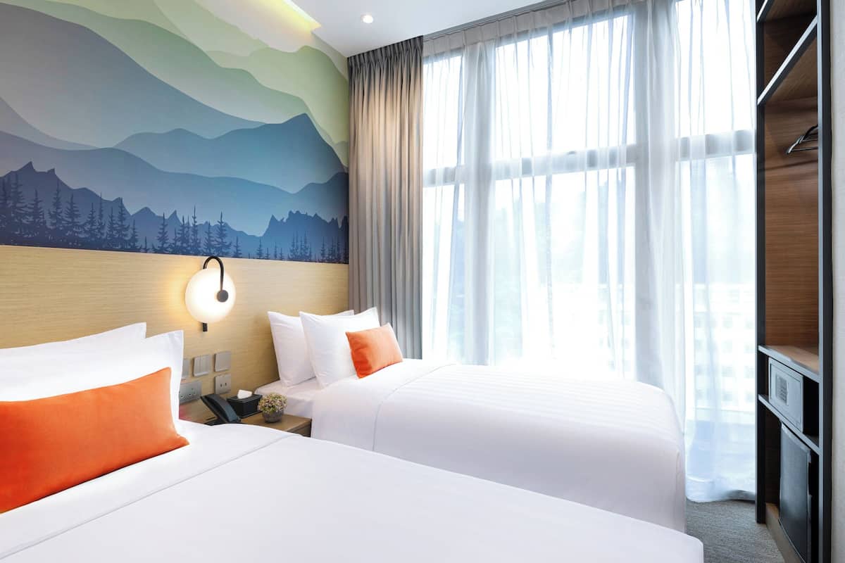 Ein Hotelzimmer mit zwei Betten, einer Wandmalerei mit Bergmotiv, einem großen Fenster mit transparenten Vorhängen und einem hölzernen Kopfteil.