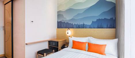 Habitación de hotel con cama, mesita de noche, escritorio y un mural en la pared que representa un paisaje de montaña.