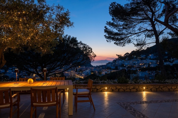 An outdoor dining area with a view of a hillside town at dusk. - Villa Alma by Elite Villas (Capri)