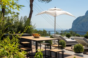 En udendørs terrasse med et træbord, lounge stole og en hvid parasol.