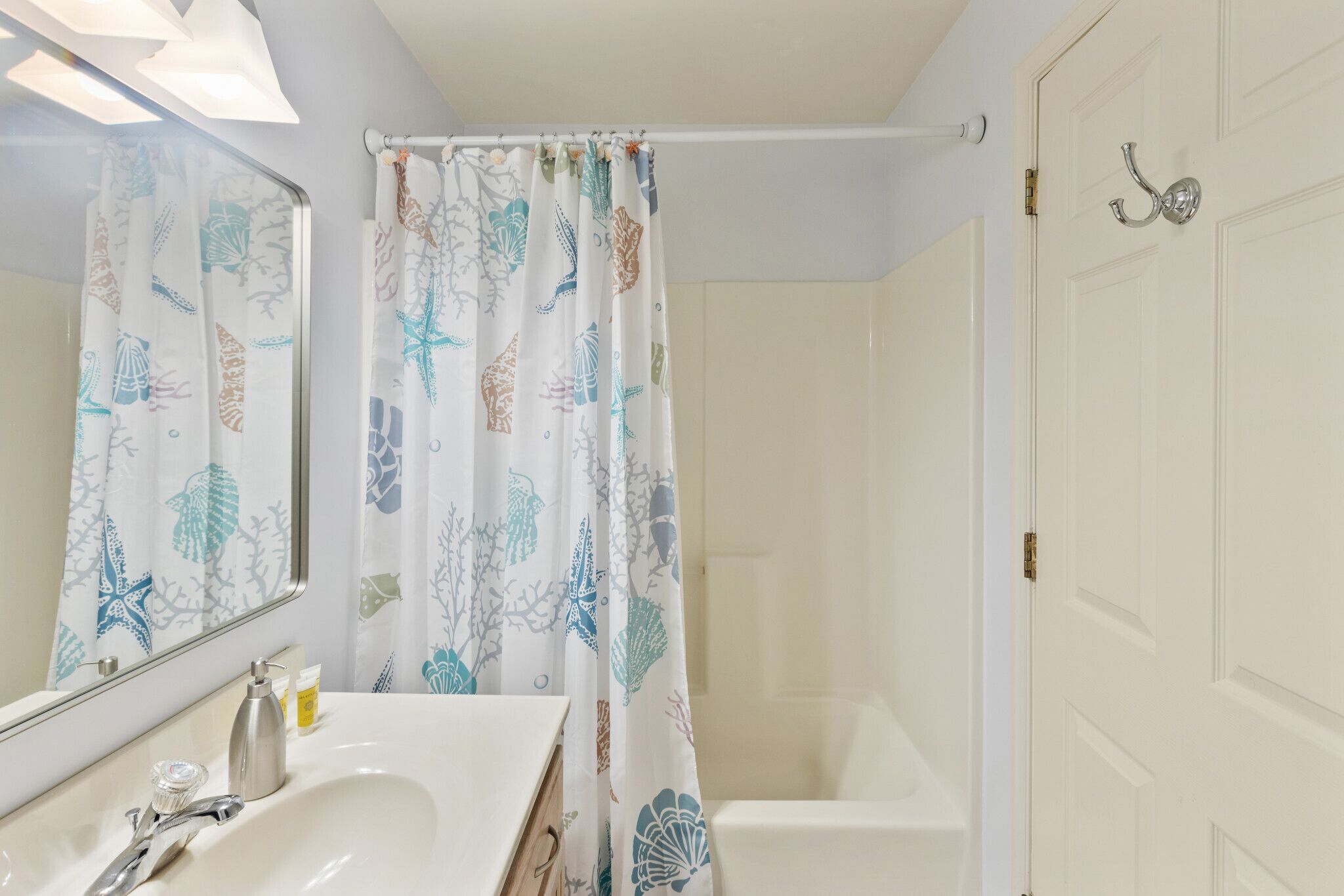 A bathroom with a white sink, mirror, and shower curtain with a leaf pattern.