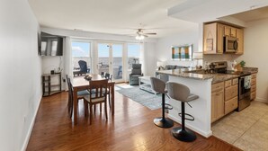 A modern kitchen with a central island, a dining area with a table and chairs, and a view through the glass doors. - Unbelievable beach views for 6 (North Beach)