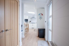 Un corridoio stretto conduce a una cucina con mobili bianchi, un forno a microonde e un'area pranzo con sedie.