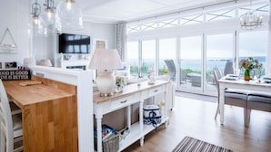 A modern kitchen with a wooden countertop, a white dining area with a table set for two, and a large sliding glass door leading to a balcony with a view of the sea. - Shearwater 30 - 2 Bedroom Lodge - Summerhill (Narberth)