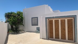 A white building with a large wooden door and a window with a decorative grille. - Villa Soliman Plage s+3 (Nabeul)