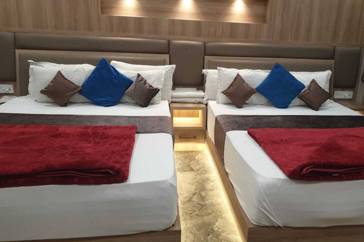 Camera d'albergo con due letti, entrambi con lenzuola bianche, cuscini marroni e blu e coperte rosse.