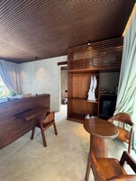Un interior moderno con un mostrador de recepción de madera, dos sillas de madera, una mesa redonda y una estantería empotrada de madera con un televisor.
