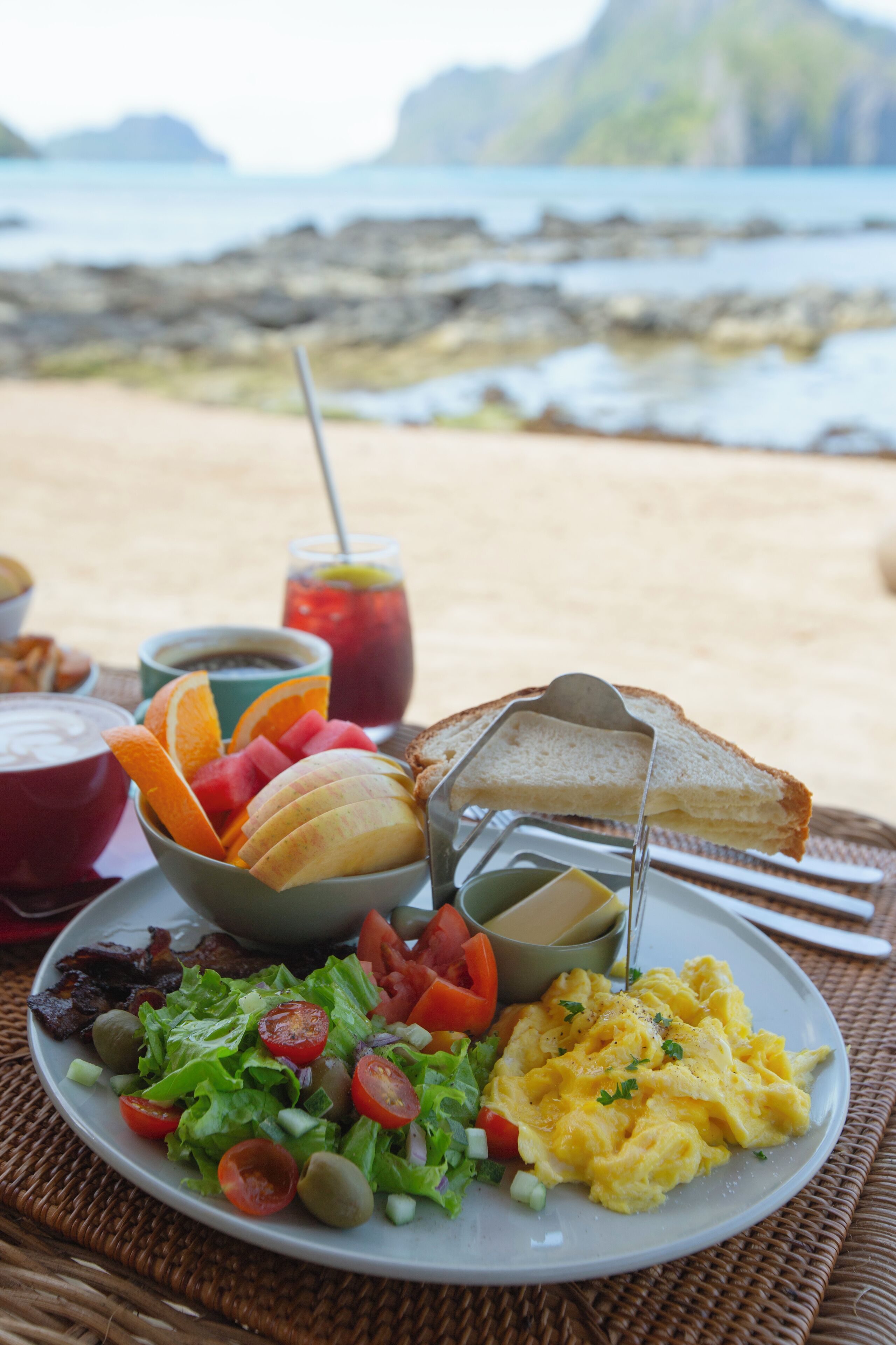 Un piatto per la colazione con pane tostato, uova strapazzate e un'insalata su un tavolino di vimini, in riva al mare.