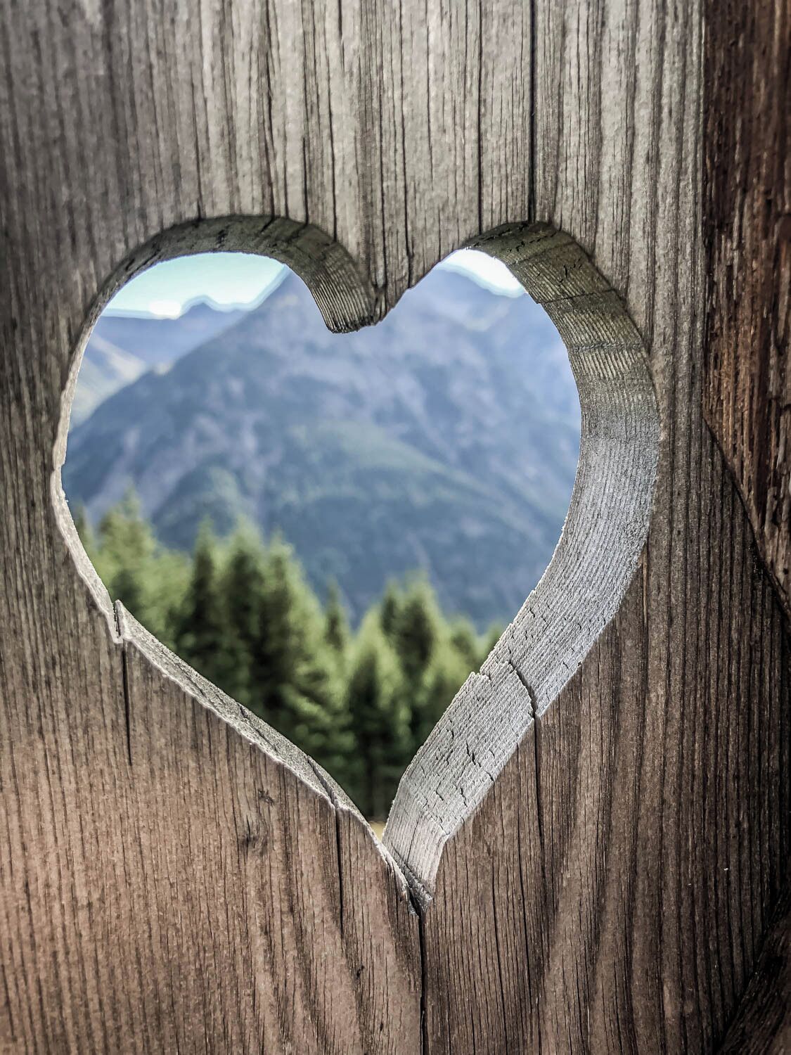 Ein herzförmiges Aussparung in einer Holzkonstruktion mit Blick auf die Berge.