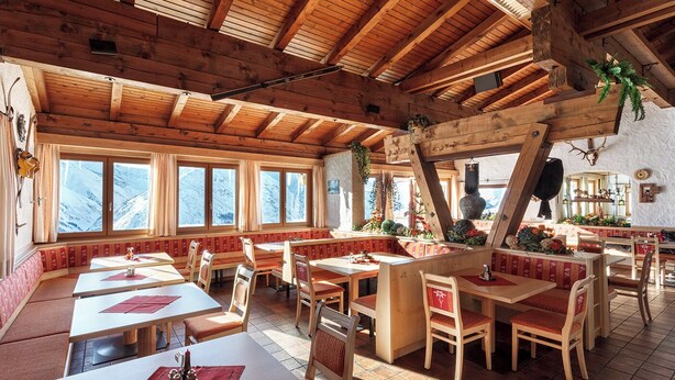 Un restaurant chaleureux avec des poutres en bois, de grandes fenêtres offrant une vue sur les montagnes et des meubles en bois de style traditionnel.