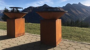 Deux barbecues d’extérieur, installés sur des supports métalliques carrés, avec une chaîne de montagnes en arrière-plan.