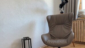 Une pièce avec un fauteuil en cuir, un tapis rond, un plancher en bois, un lampadaire noir et trois tableaux encadrés accrochés au mur.
