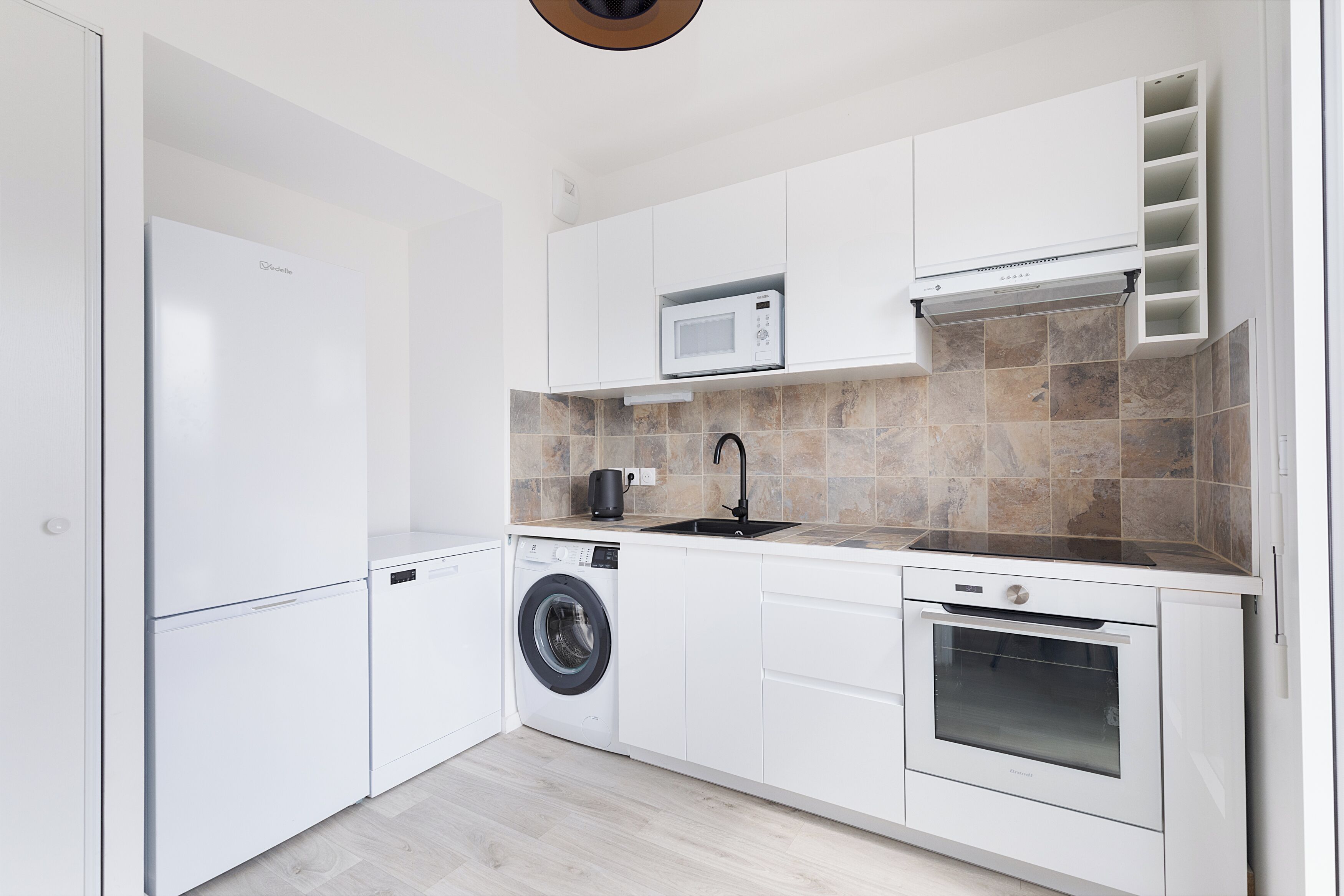 A modern kitchen with white cabinetry, a built-in washing machine, a microwave, and a stove.