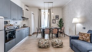 A modern kitchen with grey cabinets, a dining area with a table and chairs, and a blue sofa with a patterned pillow. - Napolehome Luxury Apartment in the center of Rome (Roma)
