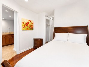 A bedroom with a wooden bed, a nightstand, a painting, and a bathroom with a shower. - Lakeview Condo - Lakefront Complex, Lake Views, Heated Pool (Big Bear Lake)