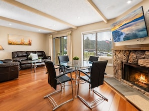A modern living room with a fireplace, a dining area with a glass table, and a sofa.