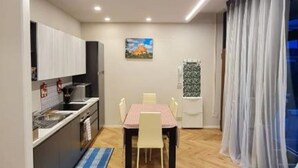 Uma cozinha compacta com eletrodomésticos modernos, uma área de jantar com mesa e cadeiras, e uma janela com cortinas leves.