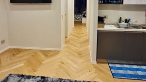 Quarto moderno e bem iluminado, com televisão de tela plana na parede, área de cozinha com pia e armários, e corredor que dá para outro cômodo.