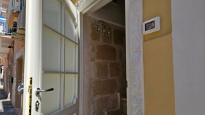 A hotel entrance with a white door, a stone wall, and a small window with a clock. - Le Camerette in Monopoli (Monopoli)