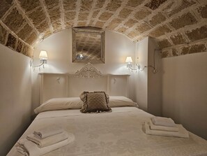 A bedroom with a brick ceiling, a bed with a quilted pillow, two wall-mounted lamps, and a mirror above the bed. - Le Camerette in Monopoli (Monopoli)