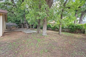 Ein Garten mit einer Holzdielen-Terrasse, einem überdachten Sitzbereich und einem großen Baum.