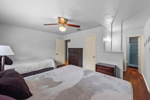 Ein Schlafzimmer mit Bett, Schminktisch, Nachttisch, Deckenventilator und einer Tür.