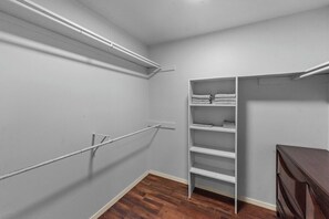 Un vestidor amplio con estantes abiertos y espacio para colgar, suelo de madera y paredes gris claro.