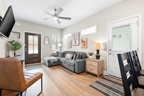 A living room with a sectional sofa, a TV mounted on the wall, a ceiling fan, and a dining area with chairs and a table. - The Rooftop Haven of Downtown (1012 Franklin St) (Clarksville)