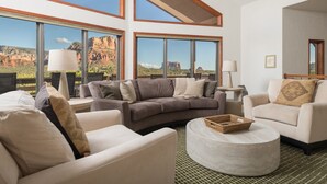 A spacious living room with a large window offering a view of red rock formations. There are two sofas, a coffee table, and a lamp. - Red Rock Vista | Incredible Views, Hot Tub, Firepit, Trails (Sedona)