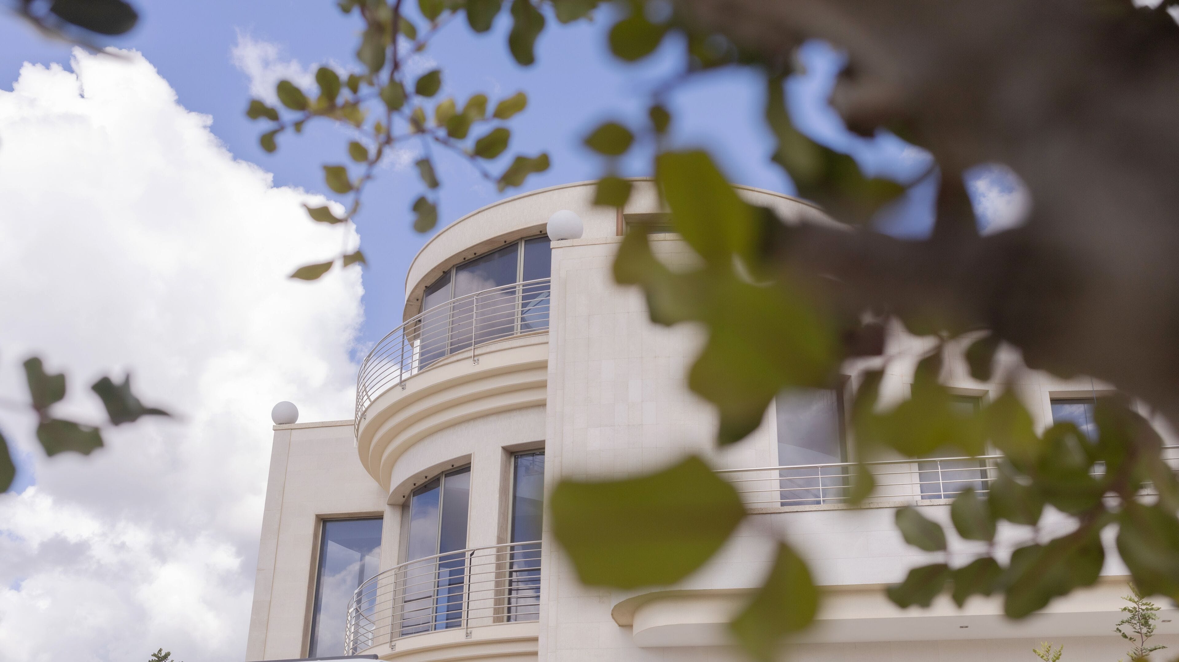 A modern building with a curved facade, large windows, and a balcony with a metal railing.