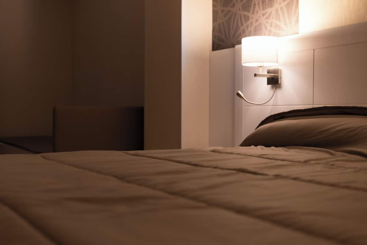 A neatly made bed with a headboard, a bedside table, and a wall-mounted lamp.
