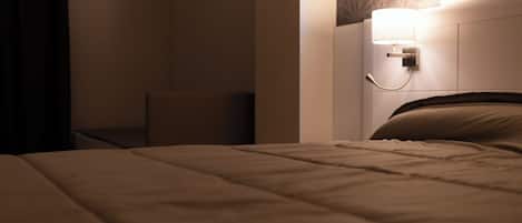 A neatly made bed with a headboard, a bedside table, and a wall-mounted lamp.