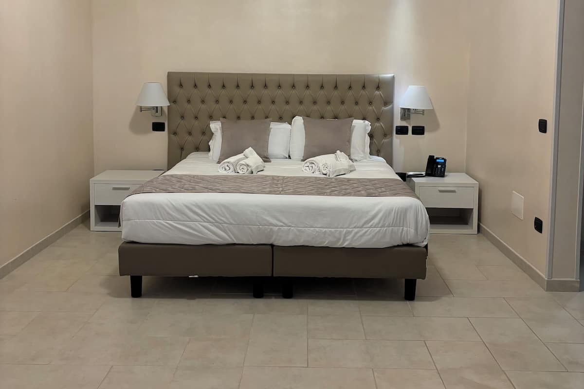 A bedroom with a large bed, two bedside tables, a headboard, and a ceiling light.