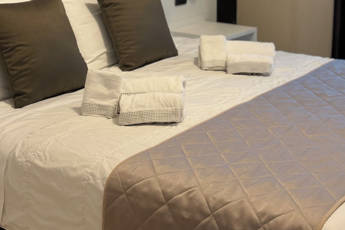 A neatly made bed with pillows, a quilted blanket, and folded towels.