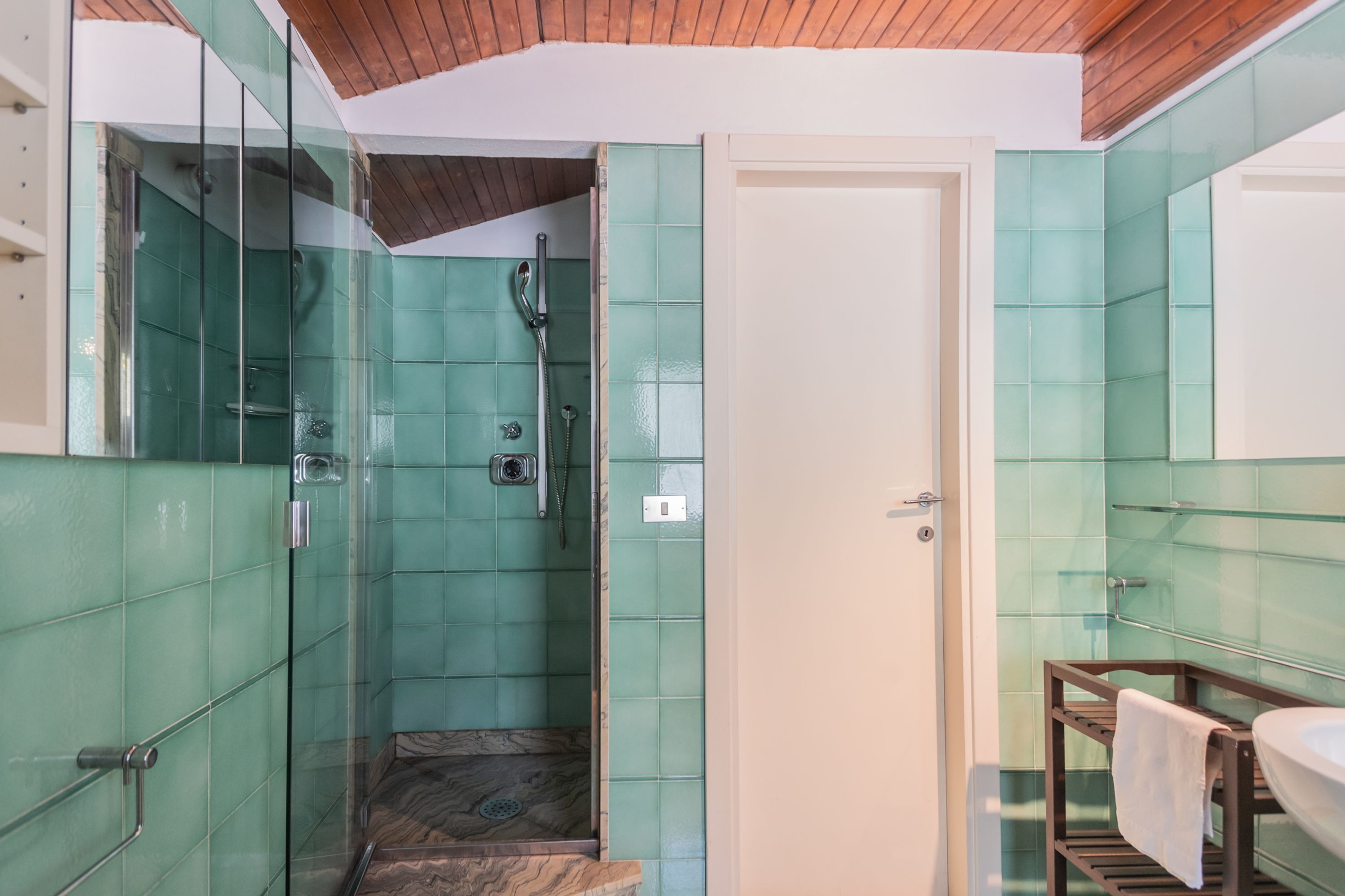 A bathroom with green tiles, a glass shower enclosure, and a wooden vanity.