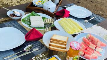 Een picknickopstelling met diverse soorten eten en bestek op een houten tafel buiten.
