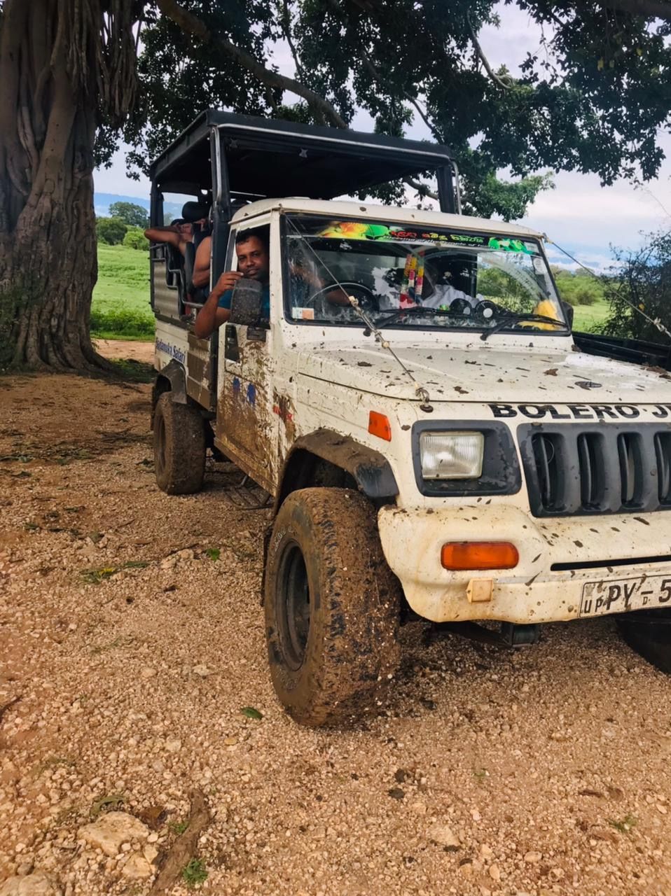 A white off-road vehicle with visible mud and wear, parked on a gravel path with trees in the background.