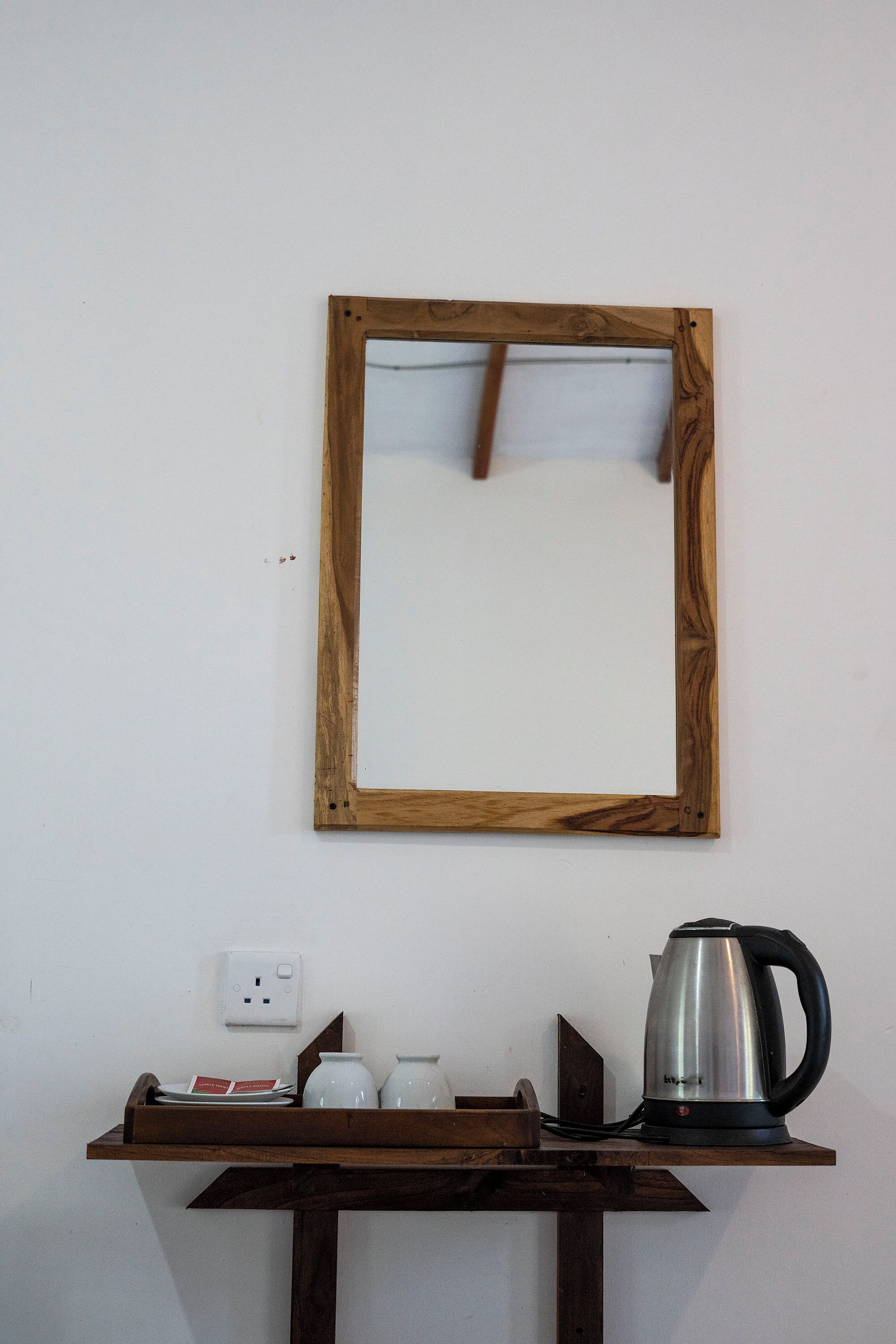 Espejo con marco de madera en una pared, repisa con tetera, tazas y un plato con un menú.