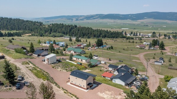 A rural area with a mix of residential houses and open fields, surrounded by forested hills.