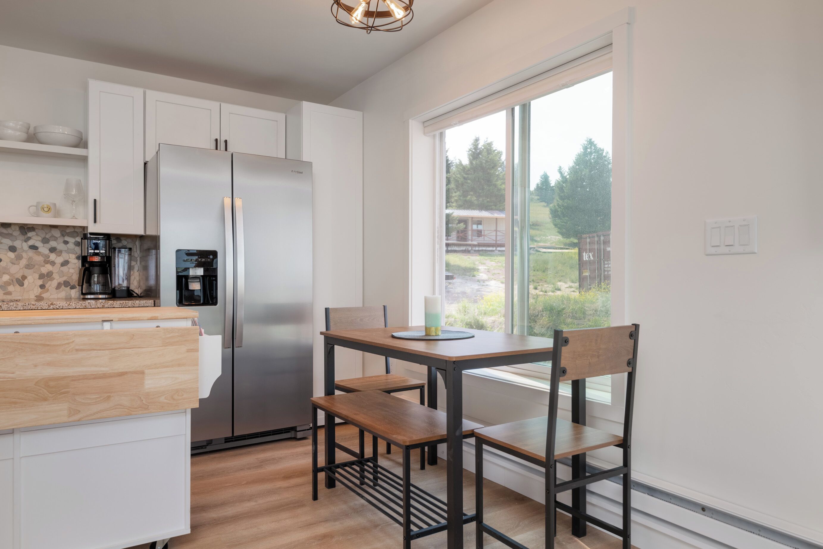 Eine moderne Küche mit weißen Schränken, einem Edelstahlkühlschrank, einer Kaffeemaschine und einem Fenster mit Blick ins Freie.
