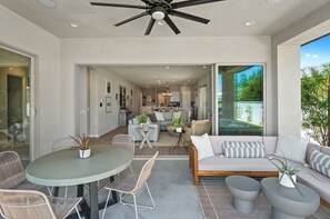 A modern living room with a ceiling fan, a dining area with a round table and chairs, and a sofa with cushions. - Saltwater Pool Haven, EV Charger, and Golf Views! (La Quinta)
