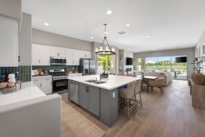 A modern kitchen with a central island, built-in appliances, and a dining area with a view. - Saltwater Pool Haven, EV Charger, and Golf Views! (La Quinta)
