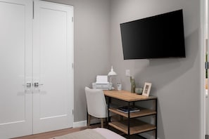 Et værelse med skrivebord, stol og et fastmonteret fladskærms-tv.