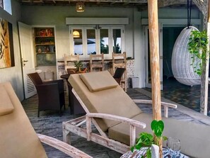 A room with a wooden-framed lounge chair, a small table with a glass, and a potted plant. - VILLA BLUE DOOR (Canggu)