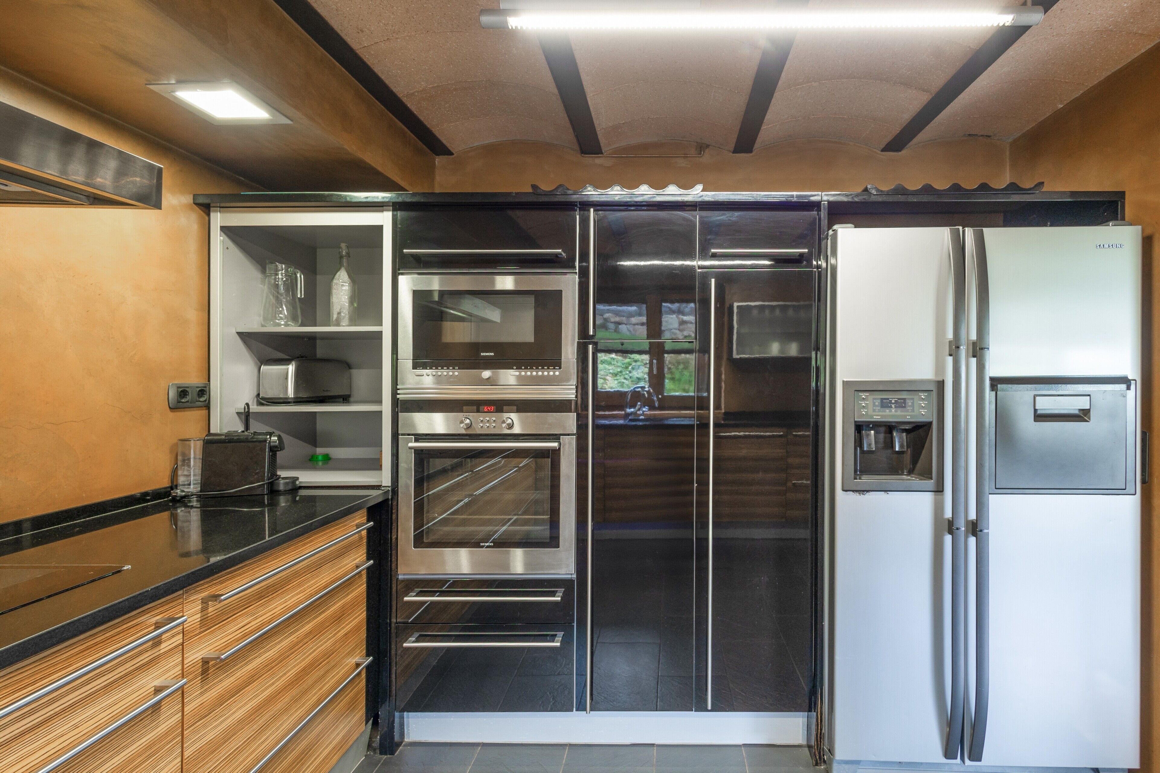 Een keuken met roestvrijstalen apparatuur, houten kastjes en een zwart aanrecht.