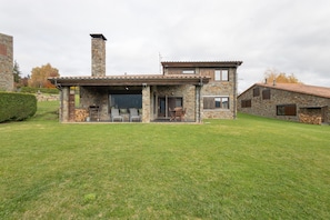 Une maison en pierre dotée d’un patio couvert, d’une cheminée et d’une pelouse bien entretenue.
