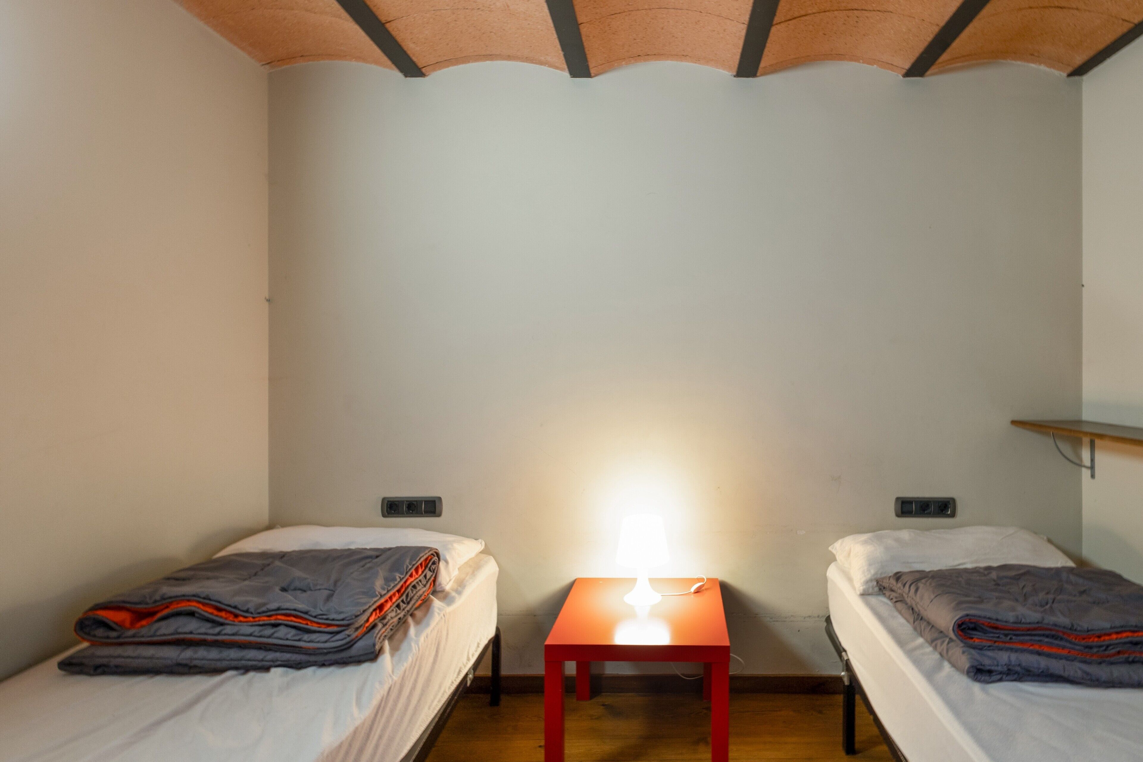 Una habitación pequeña con dos camas, una mesita de noche y un estante.